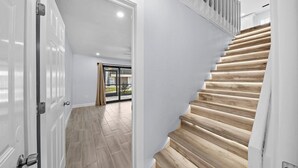 Ein modernes Interieur mit einer Holztreppe, weißen Wänden und Blick durch eine Glastür in einen Außenbereich.