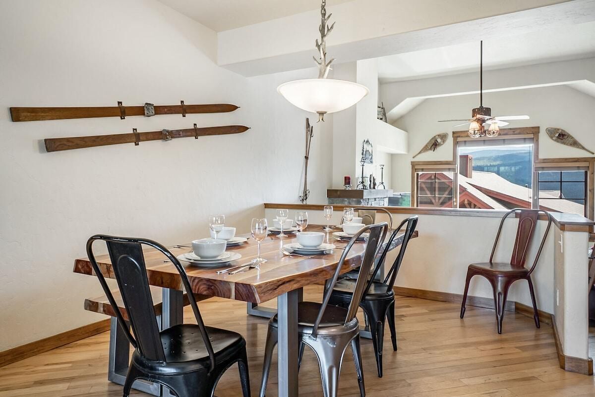 Een eetruimte met een houten tafel voor zes personen, metalen stoelen, een kroonluchter en ski's die aan de muur zijn bevestigd.