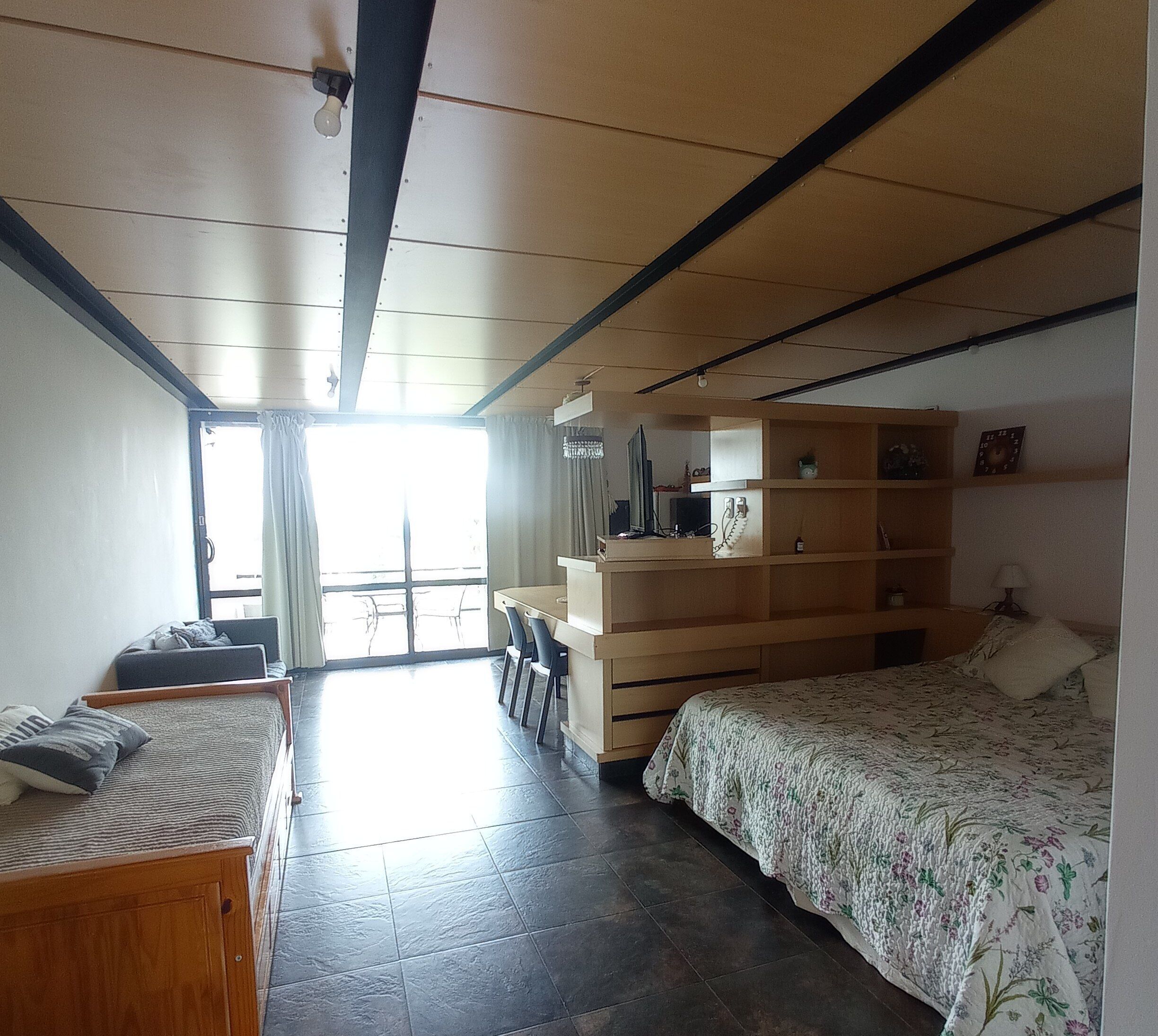 Un dormitorio con cama, escritorio, silla, armario y ventana.