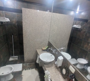 A bathroom with a large mirror, two sinks, a shower, and a toilet.