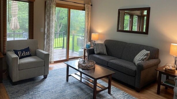 Una sala de estar con sofá, sillón y mesa de centro, un balcón con vistas y un espejo en la pared.