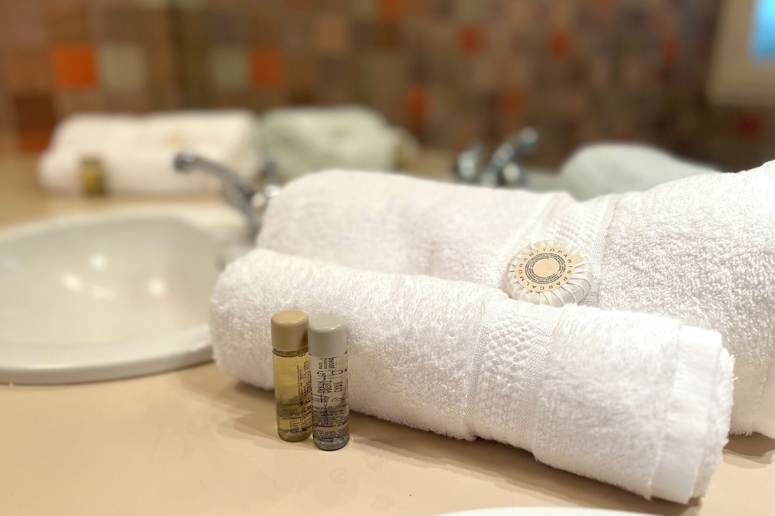 A bathroom with a white sink, two bottles of toiletries, and a folded white towel with a decorative emblem.