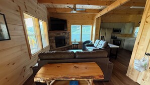 A cozy cabin interior with a stone fireplace, wooden furniture, and a kitchen area. - Brand new cabin with HOT TUB, Dock & Lake Access (Butler)