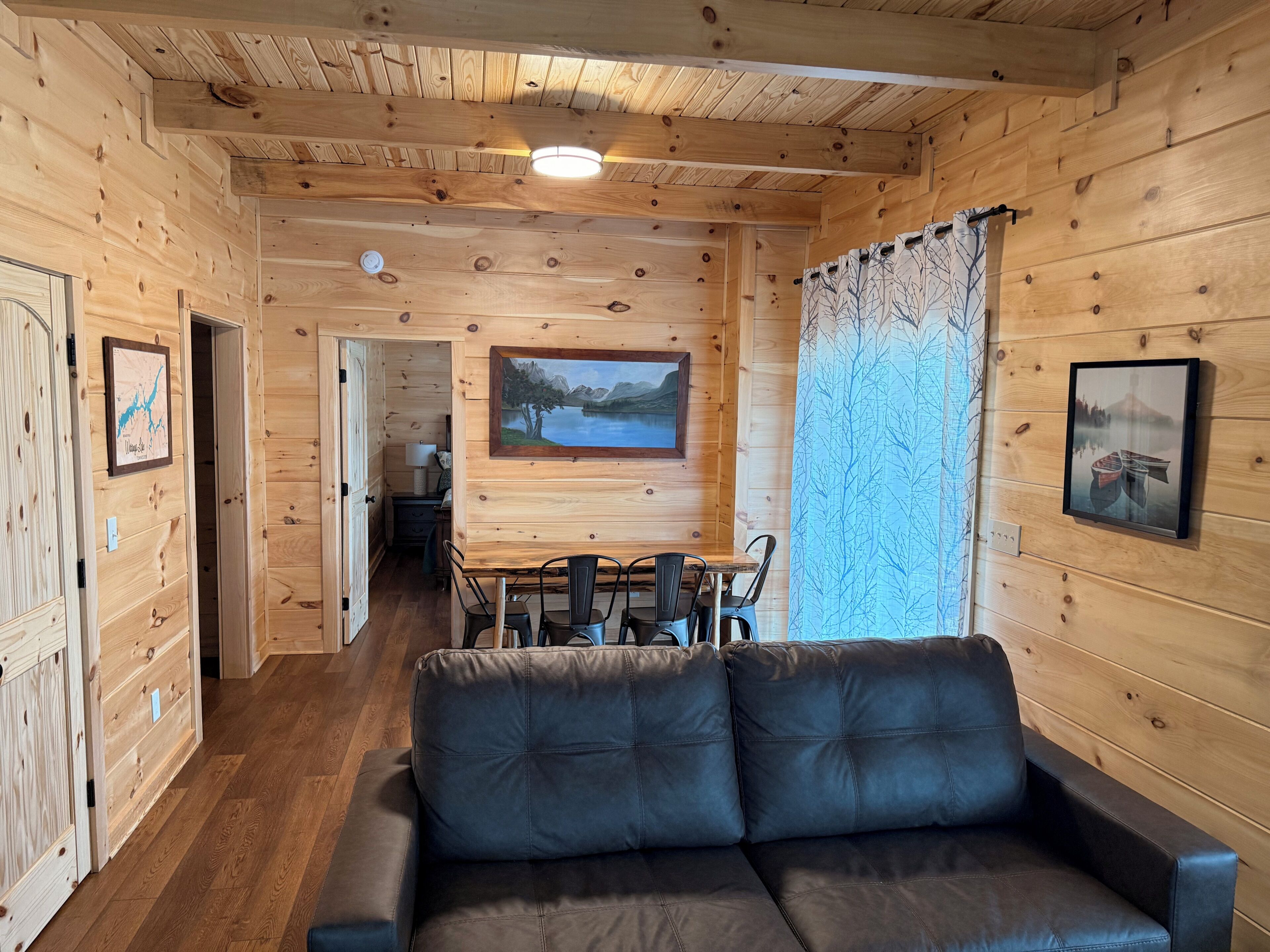 Een houten blokhut interieur met een eethoek, een bank en kunstwerken in lijsten aan de muren.