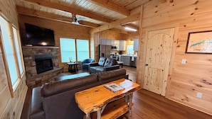 A cozy cabin interior with a stone fireplace, a wooden dining table, a sofa, and a kitchen area. - Brand new cabin with HOT TUB, Dock & Lake Access (Butler)