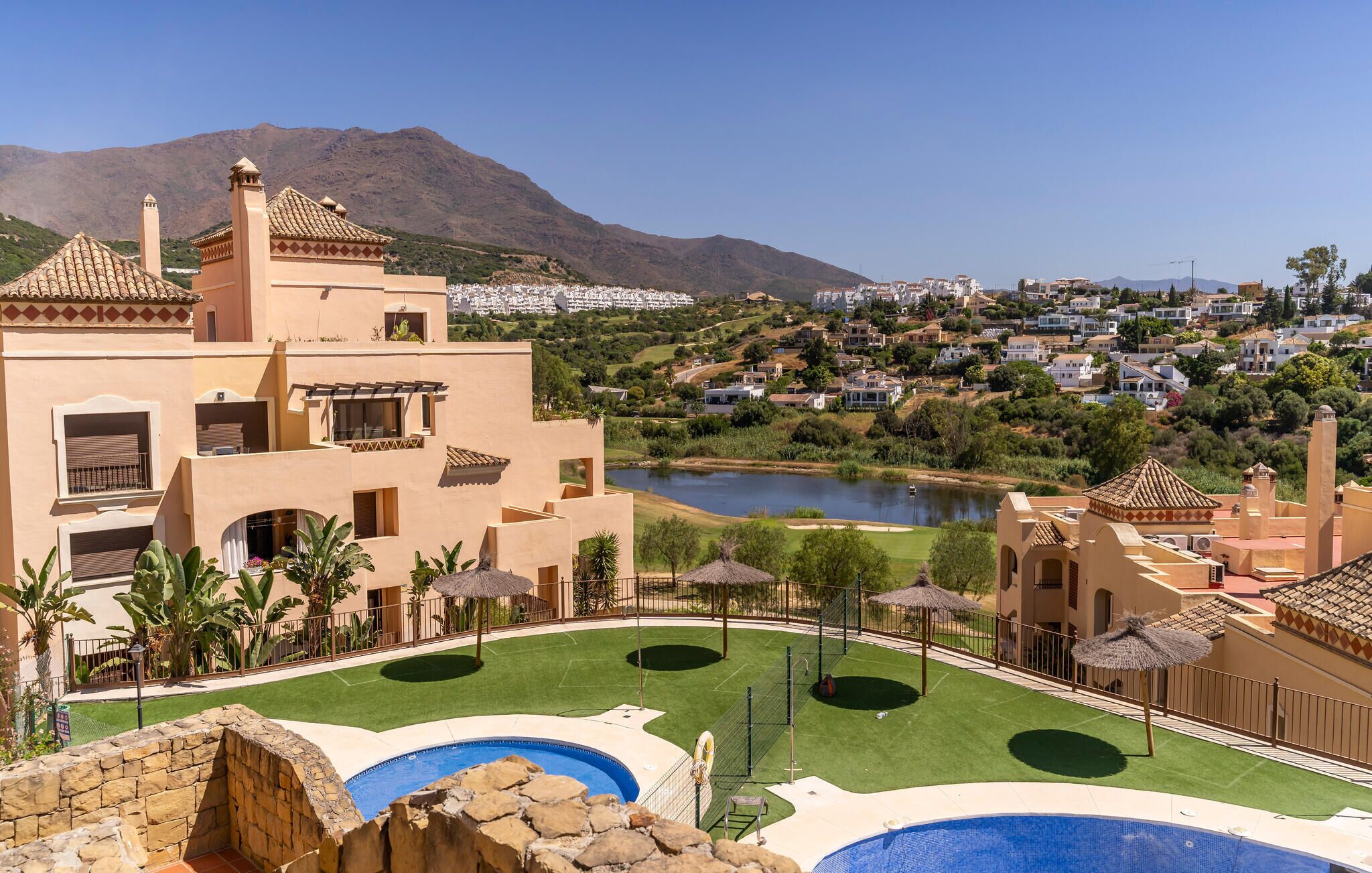 A resort with multiple swimming pools, a tennis court, and a view of a lake and town in the background.