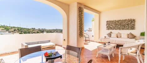A spacious balcony with a glass table and chairs, a sofa, and a decorative wall piece.