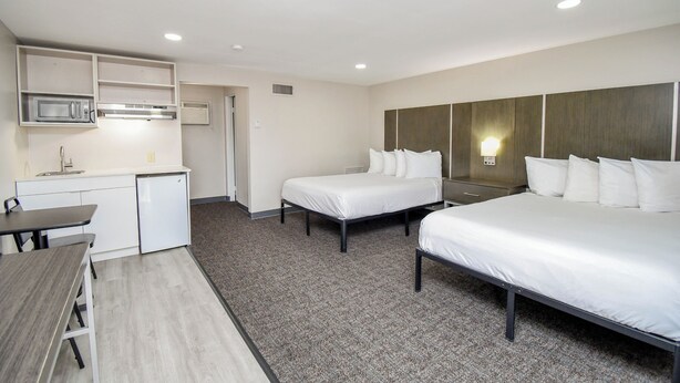 Habitación de hotel con kitchenette, dos camas individuales, escritorio y una pequeña mesa de comedor.