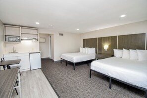 Habitación de hotel con kitchenette, dos camas individuales, escritorio y una pequeña mesa de comedor.