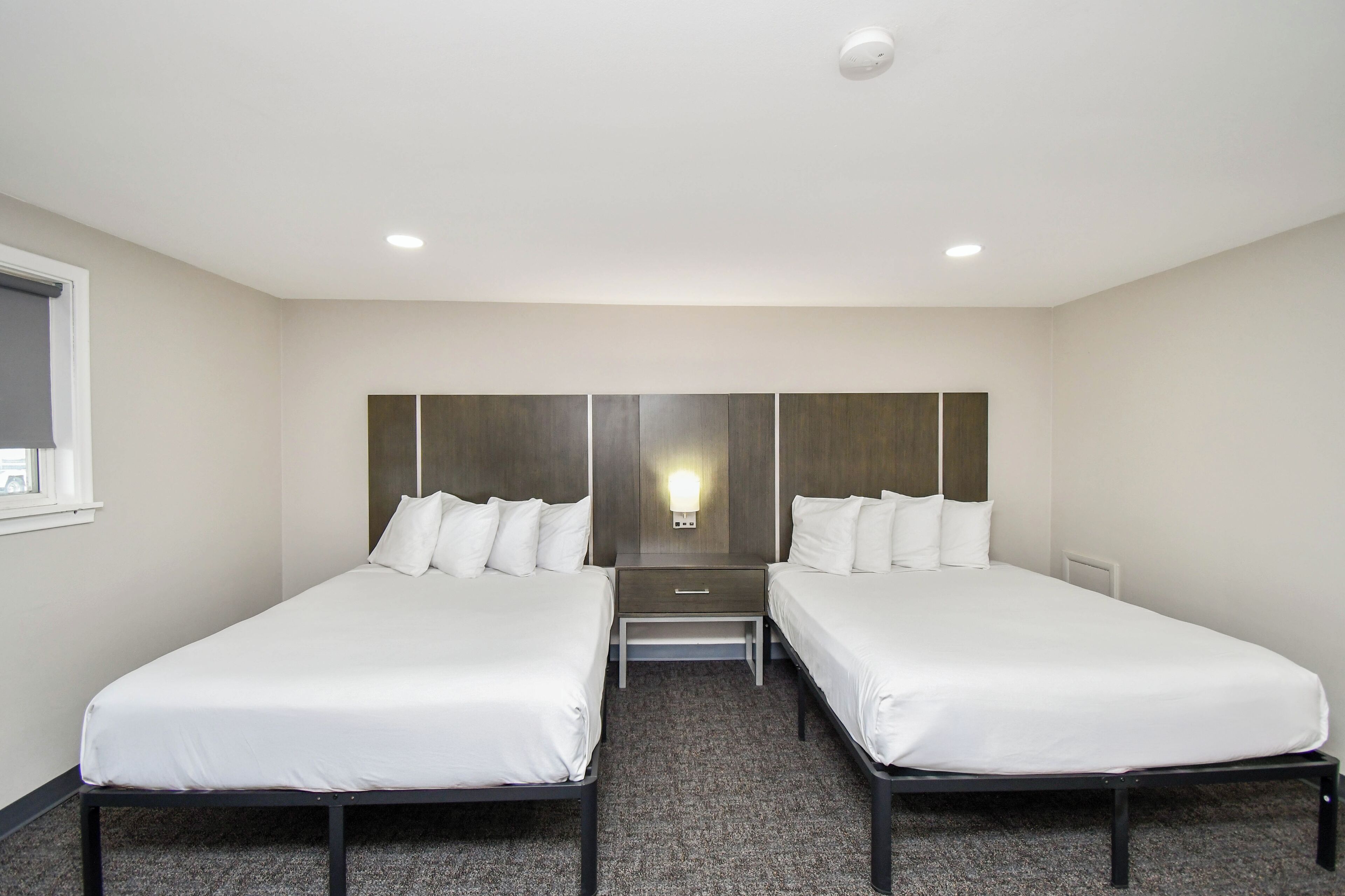 Habitación de hotel con dos camas individuales, una mesita de noche y una lámpara fijada a la pared.
