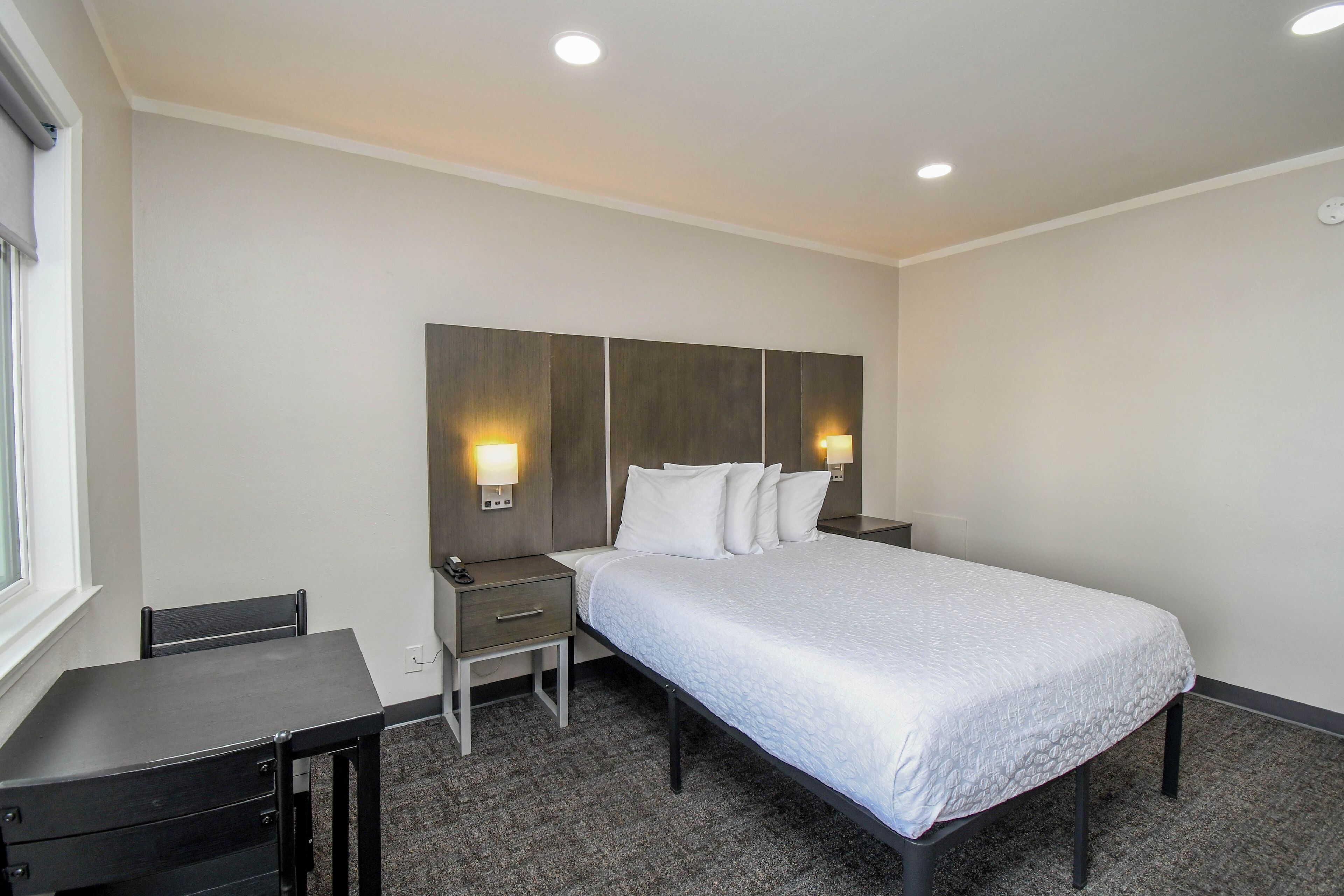 Una habitación de hotel con cama, mesitas de noche, escritorio y una silla.