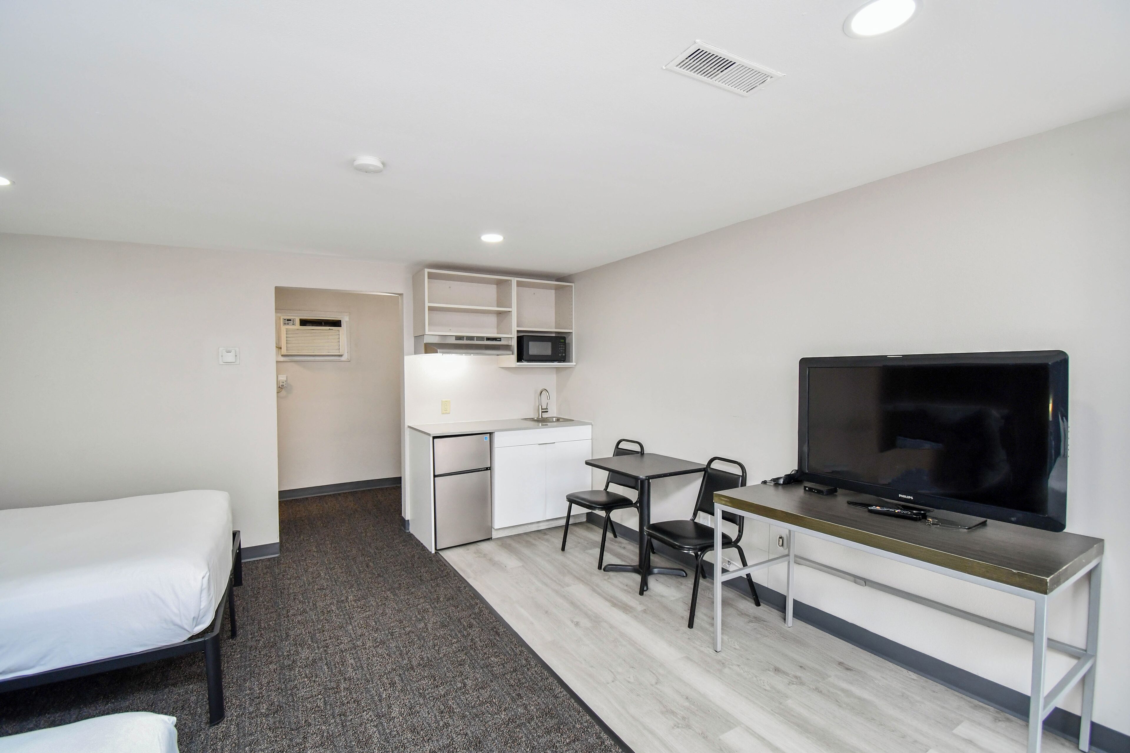 A compact hotel room with a single bed, kitchenette, and a TV.