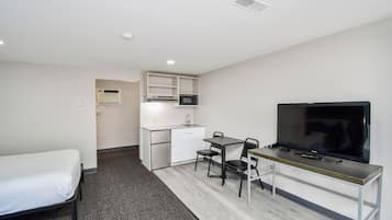 A compact hotel room with a single bed, kitchenette, and a TV.