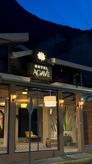 Hotel Agave, un hotel con un llamativo letrero iluminado, amplias ventanas y vistas a las montañas al fondo.
