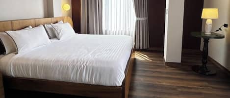 Una habitación de hotel con una cama grande, un televisor montado en la pared y una mesita de noche con una lámpara.
