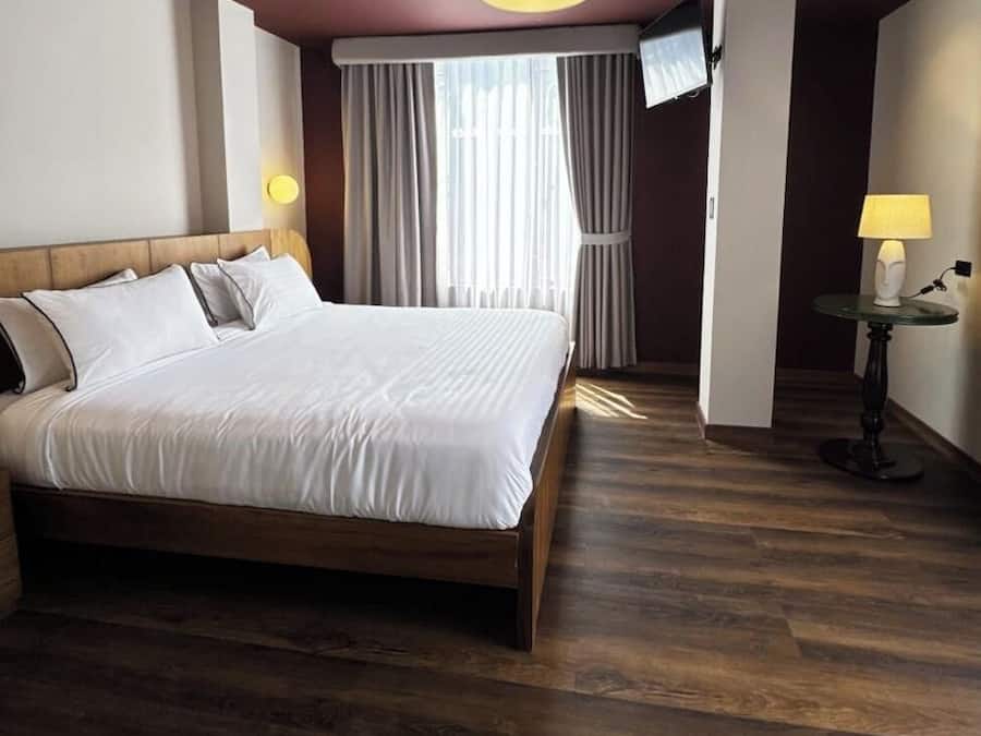 A hotel room with a large bed, a television mounted on the wall, and a small table with a lamp.