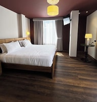 Una habitación de hotel con una cama grande, un televisor montado en la pared y una mesita de noche con una lámpara.