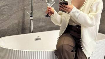 Une personne assise près d’une baignoire, avec un robinet, tenant un verre et un téléphone intelligent.