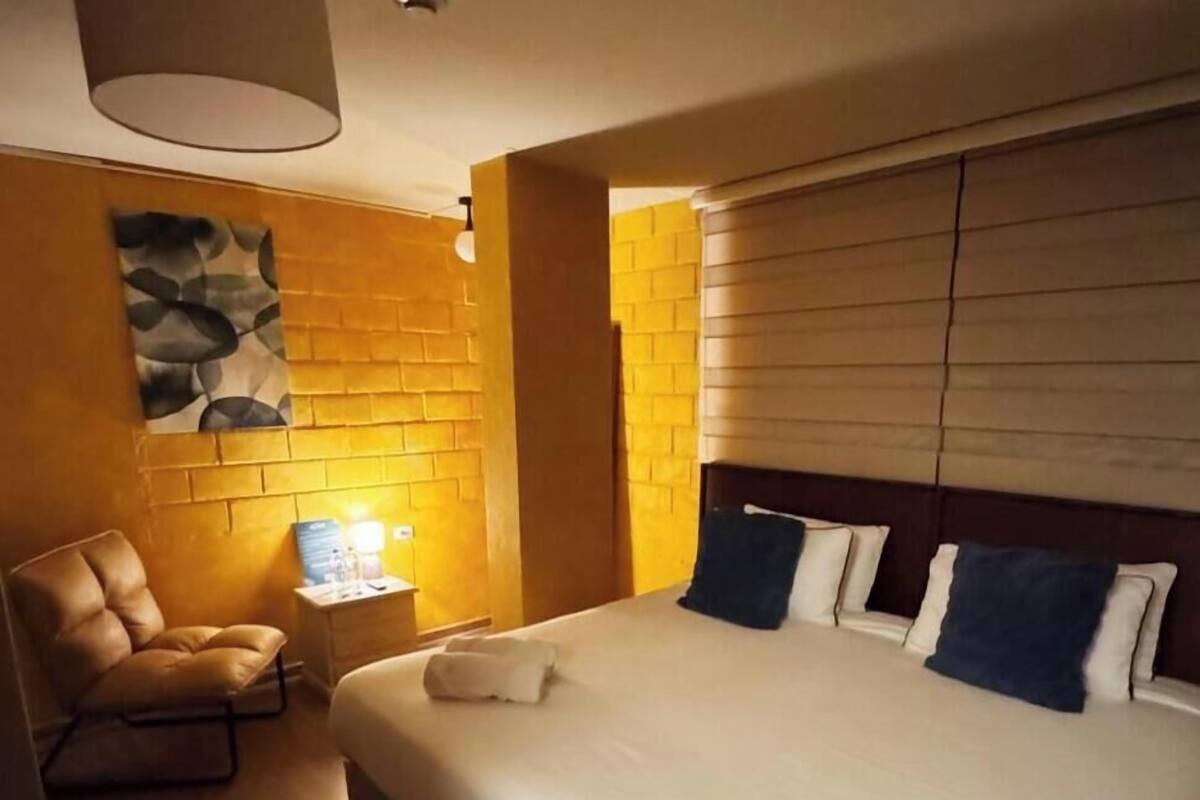 Una habitación de hotel con una cama grande, una silla, una mesita de noche y una lámpara fijada a la pared.