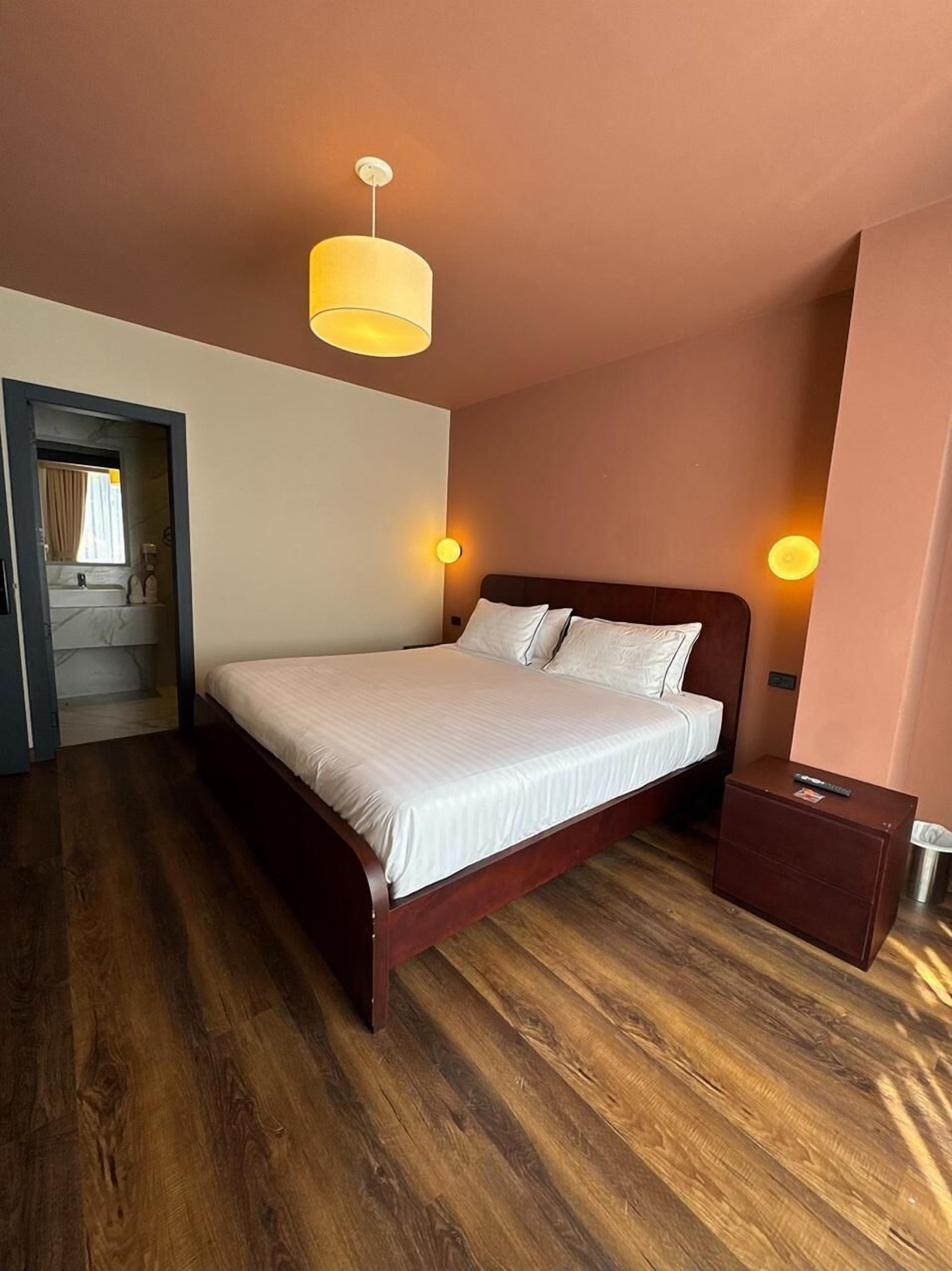 Un dormitorio con una cama de madera, dos lámparas de noche, una mesita de noche y una puerta que da al baño.
