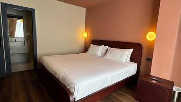 Un dormitorio con una cama de madera, dos lámparas de noche, una mesita de noche y una puerta que da al baño.