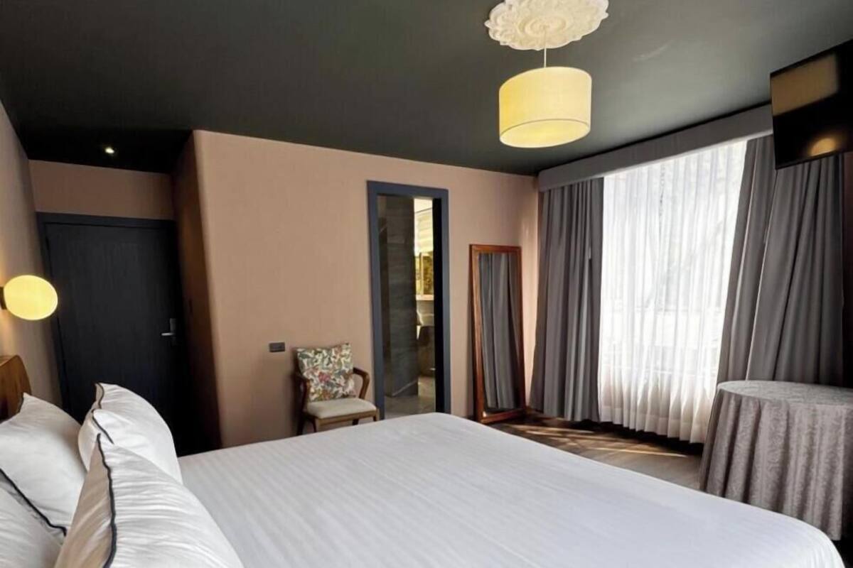 Habitación de hotel con una cama grande, una silla, un espejo y vistas al exterior.