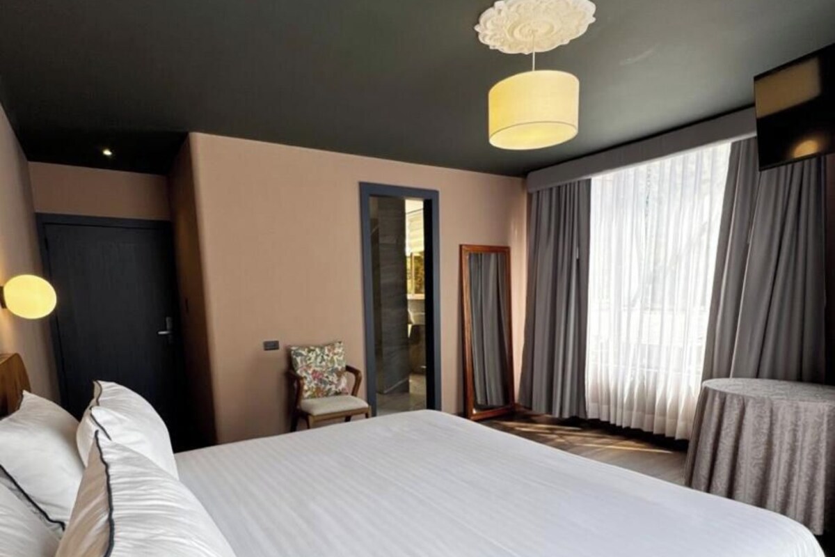 Habitación de hotel con una cama grande, una silla, un espejo y vistas al exterior.