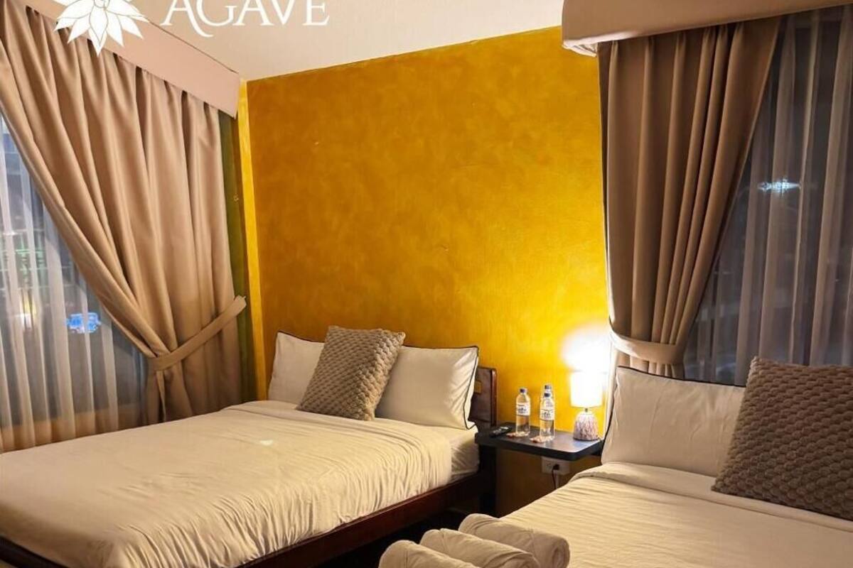 Una habitación de hotel con dos camas, una mesita de noche, una lámpara y una ventana con cortinas.