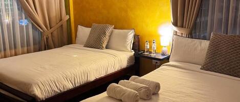 A hotel room with two beds, a nightstand, a lamp, and a window with curtains.