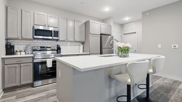 Una cocina moderna con electrodomésticos de acero inoxidable, una isla central con taburetes de bar y armarios en color gris claro.