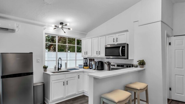 Una cocina moderna con armarios blancos, un refrigerador de acero inoxidable, un microondas y una barra con taburetes.