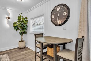 A dining area with a round table, two chairs, a potted plant, a wall clock, and a window with blinds. - Cozy Private Cottage, Minutes to Anna Maria Island (Bradenton)