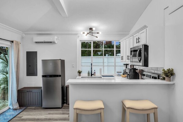 A modern kitchen with a central island, stainless steel appliances, and a large window providing natural light. - Cozy Private Cottage, Minutes to Anna Maria Island (Bradenton)