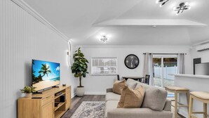 Una sala de estar moderna con televisor, mueble de madera para entretenimiento, sofá color beige y una planta grande en maceta.