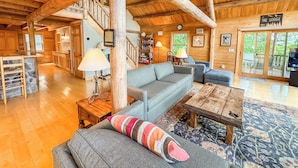 A spacious living area with a wooden ceiling, a stone bar, a grey sofa, and a patterned rug.