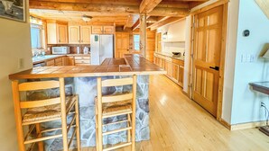 A spacious kitchen with wooden cabinets, a central island with bar stools, and a stone backsplash.