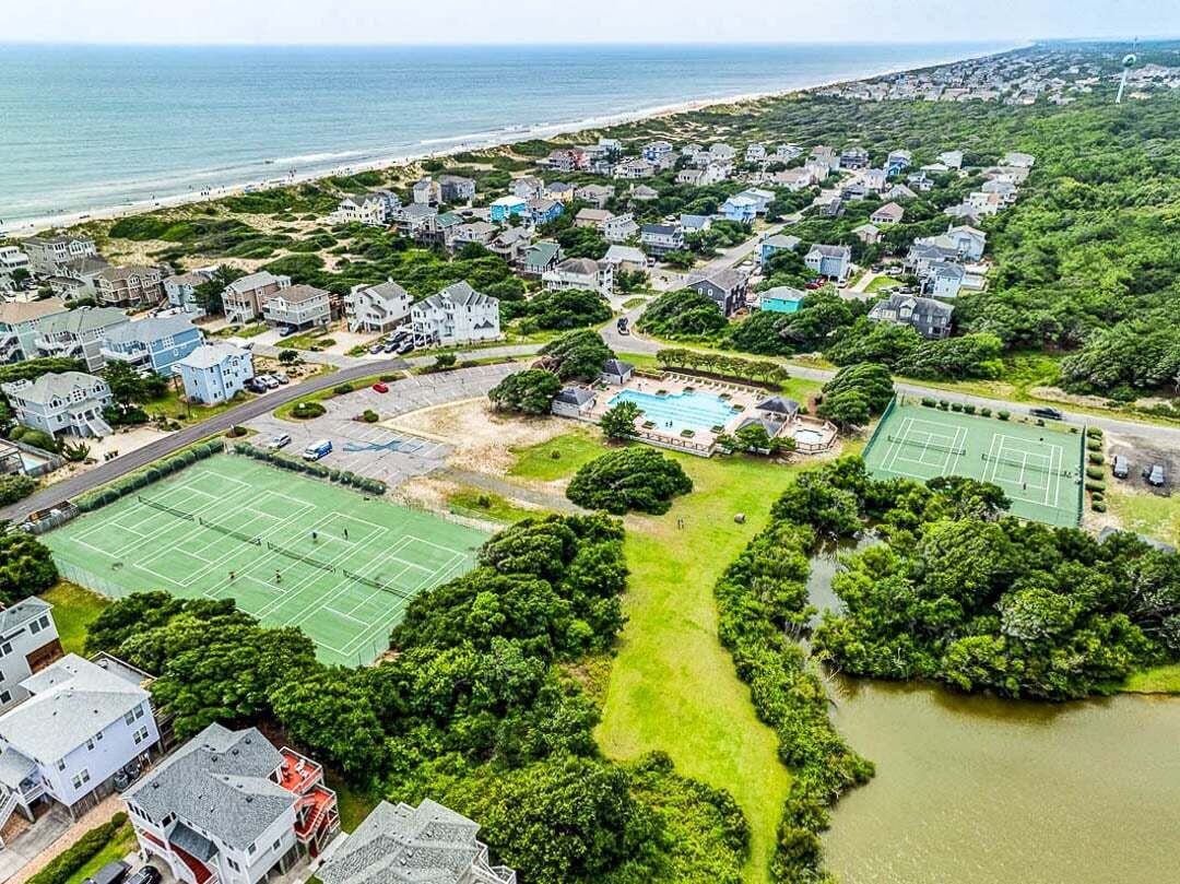 Vista aérea de una zona residencial costera con casas, una cancha de tenis y una piscina.