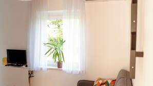 A living room with a sofa, a television, a potted plant, and a window with curtains. - Modern Family Apartment • AC • Free Parking • EV Charging  / Gorishka4Three (Ljubljana)