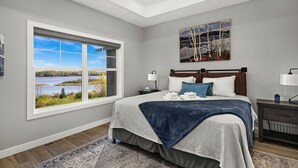 Ein Schlafzimmer mit einem großen Fenster, einem Bett mit blauer Decke, einem Nachttisch und einem Gemälde an der Wand.