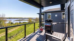 Eine überdachte Terrasse mit Grill und Sitzgelegenheiten, mit Blick auf einen See und eine Rasenfläche.