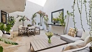 Ein moderner, minimalistischer Wohnraum mit einem runden Holztisch, einem weißen Sofa und verschiedenen Kübelpflanzen.
