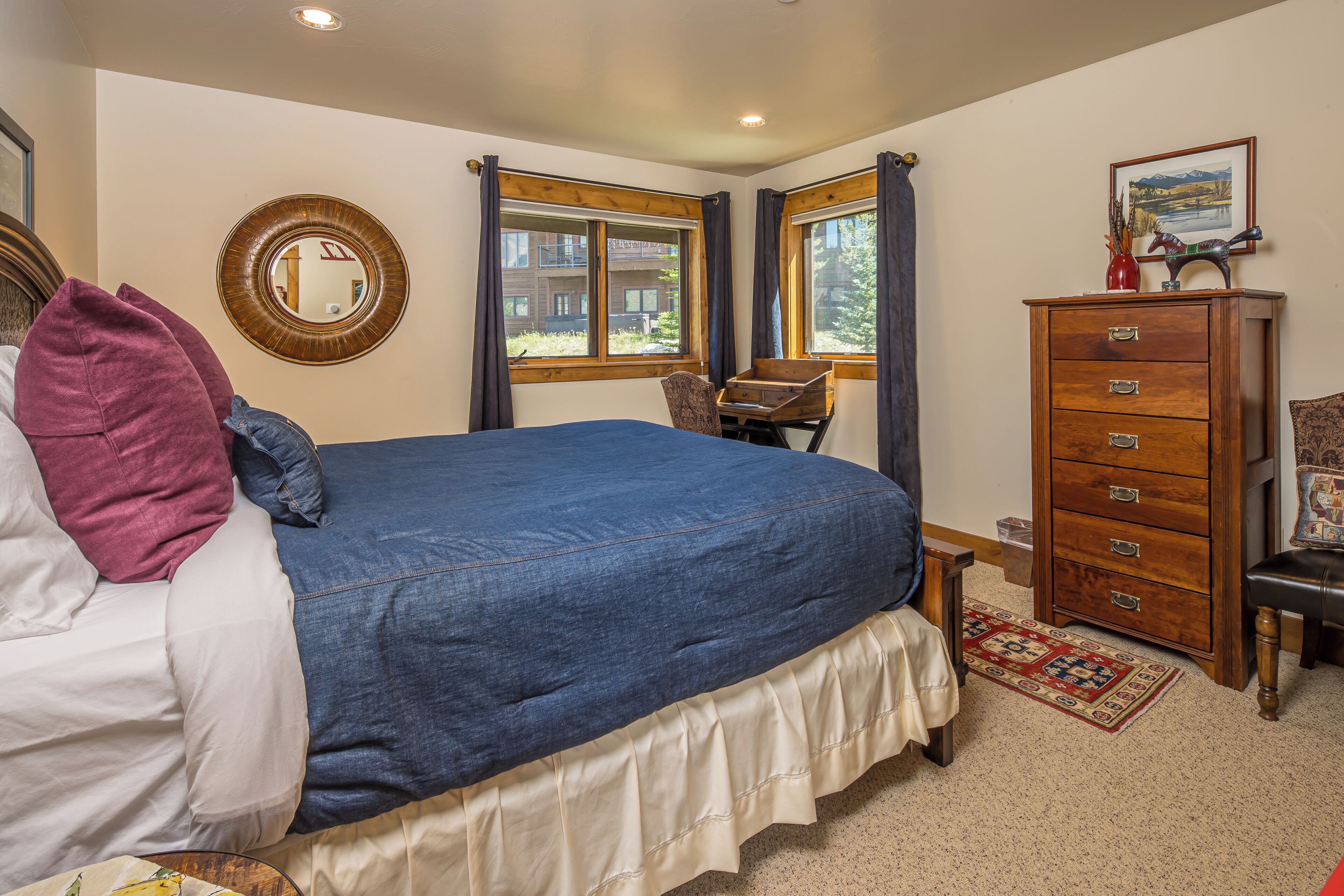 Une chambre à coucher avec un grand lit, une commode en bois, une chaise et une fenêtre donnant sur des immeubles.