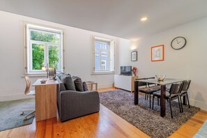 A modern living room with a sofa, a dining table with chairs, a small TV, and a clock on the wall. - Cozy Apartment in Downtown Porto (Porto)
