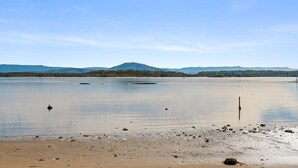 A calm lake with a sandy beach and a distant mountain range.