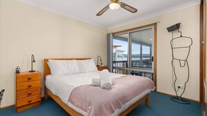 A bedroom with a wooden bed, a nightstand, a desk lamp, a wall-mounted TV, and a balcony with a view.