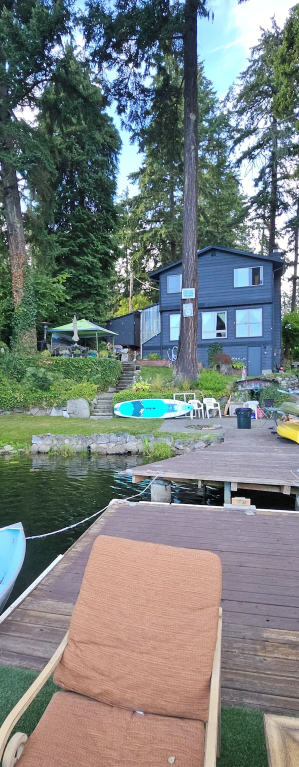 A wooden deck with a lounge chair, a small boat, and a dock extending into a body of water.