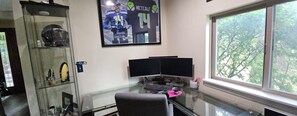 Ein Homeoffice mit Schreibtisch, zwei Monitoren, Tastatur, Stuhl und Fenster mit Blick auf Bäume.