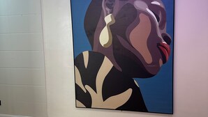 Una obra de arte moderna sobre una pared blanca, piso de madera y lámpara de techo.