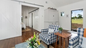 A room with a checkered sofa, a wooden table, and a view of a grassy field through a glass door.
