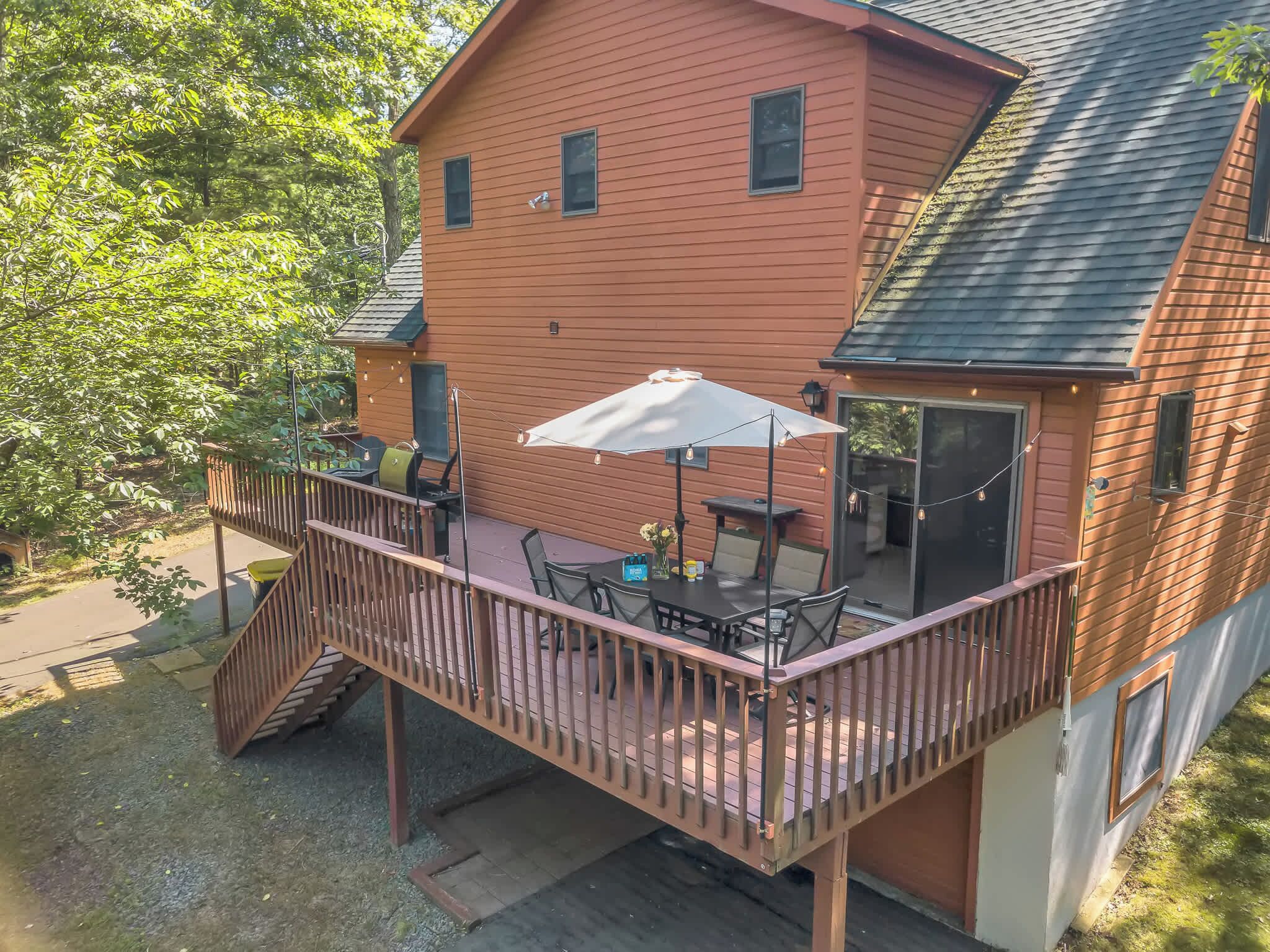 A two-story house with a deck, a patio with outdoor furniture, and a large sliding glass door.